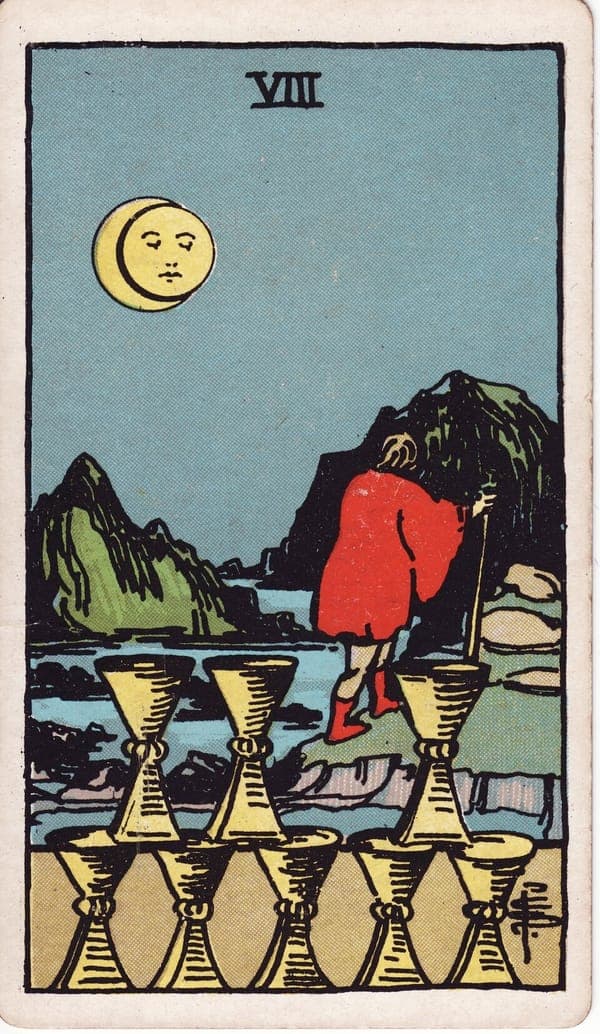 Eight of Cups tarot card: Under an eclipsed moon with a watching face, a cloaked figure walks away up rocky ground, staff in hand, toward mountains.