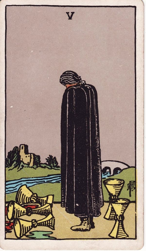 Five of Cups tarot card: A figure in a long black cloak stands head-bowed before three overturned cups, their contents soaked into the ground.