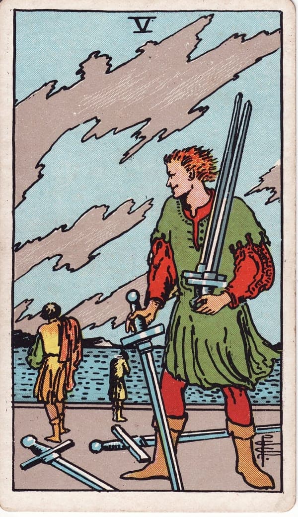 Five of Swords tarot card: Under a torn, windswept sky, a smirking figure gathers three swords, two more at his feet, watching two others walk away toward a rough sea — one with face in hands.