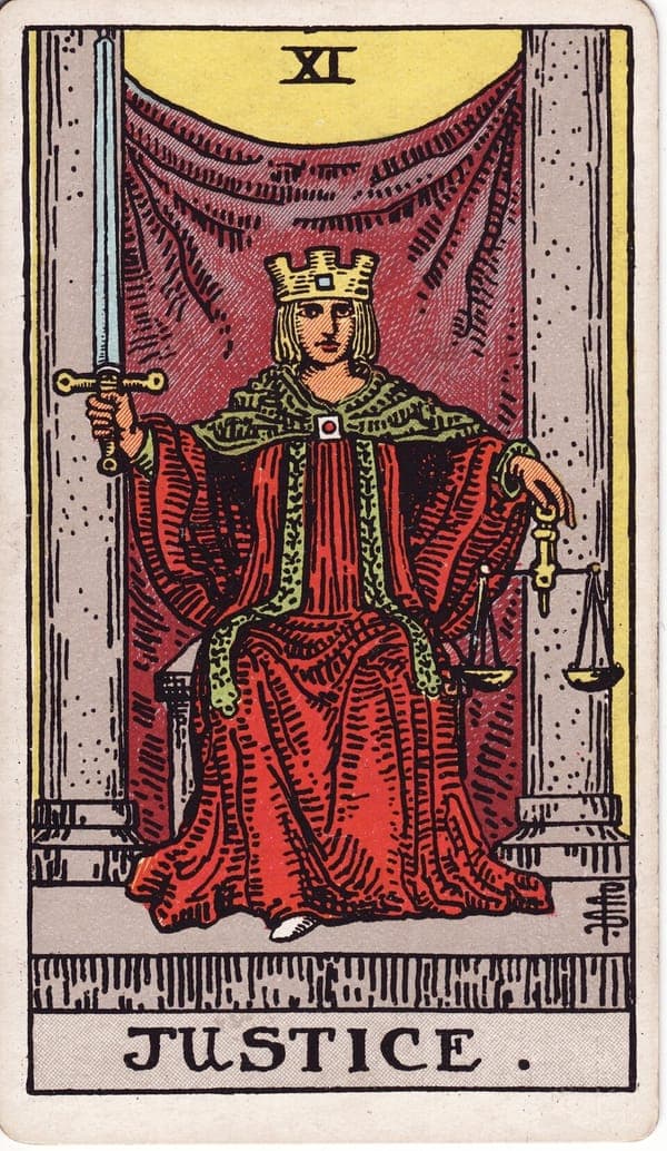 Justice tarot card: A crowned figure sits between two pillars holding an upright sword in one hand and balanced scales in the other — clarity and equity inseparable.