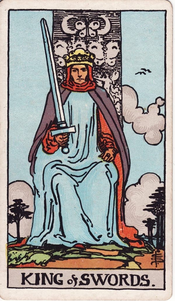 King of Swords tarot card: A stern king faces forward on a stone throne carved with butterflies and crescent moons, his sword upright but tilted a few degrees from vertical — justice with a margin for mercy.