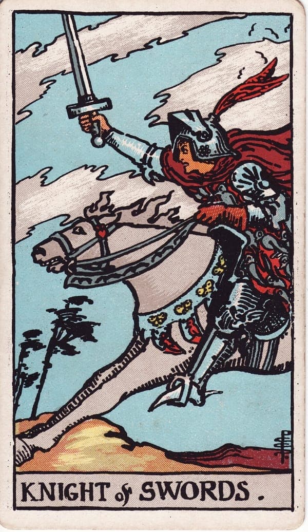 Knight of Swords tarot card: A knight at full gallop leans into the wind, sword thrust high, cloak and plume streaming; his white horse's mane whips sideways and its eyes roll with the pace.