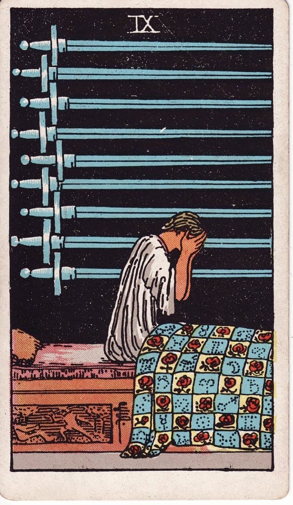 Nine of Swords tarot card: A figure sits bolt upright in bed, face buried in both hands, in a room of total black.