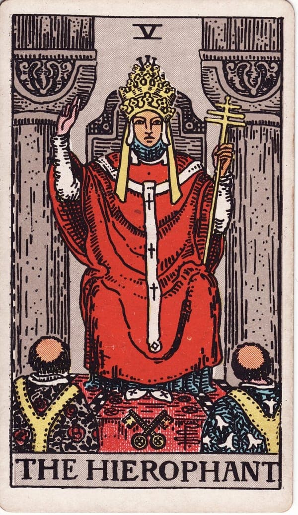 The Hierophant tarot card: A robed religious figure sits between two pillars — echoing The High Priestess, but in a public temple rather than a hidden one.